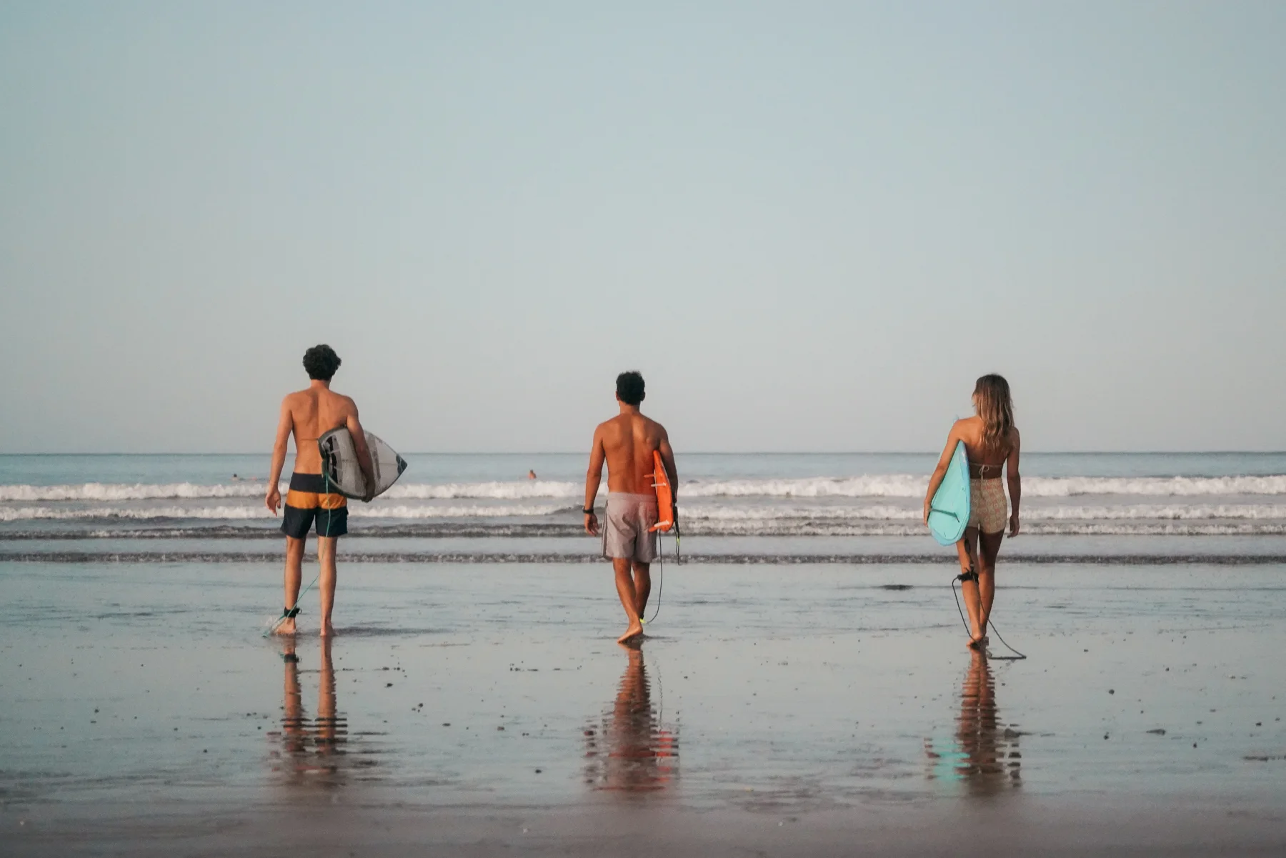 Three surfers walking into the water together, boards under their arms