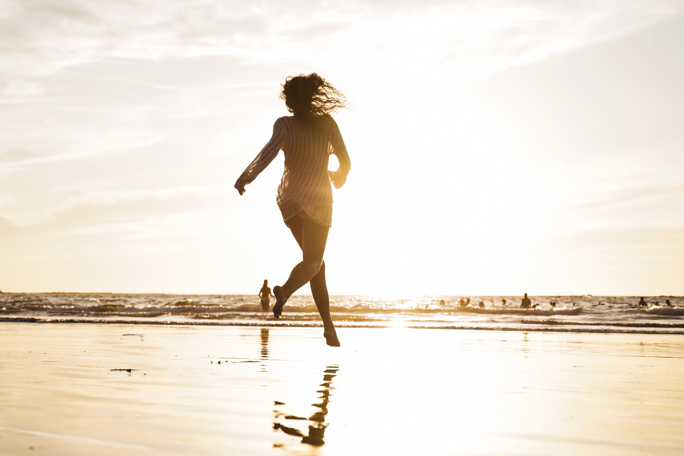 A woman running along the shoreline into the golden light at sunset