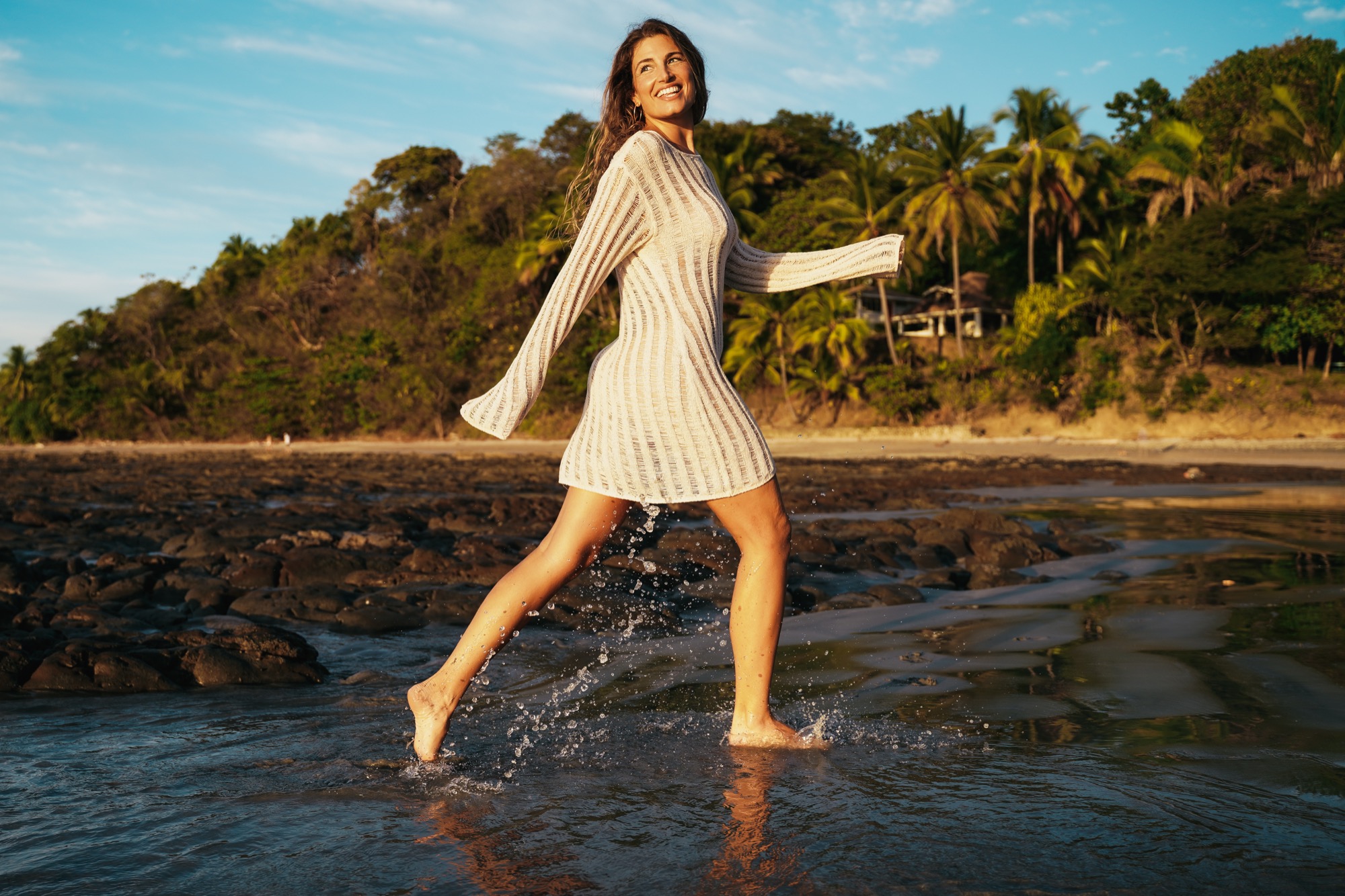 A woman walking barefoot through the shallows below the jungle at golden hour in Nosara