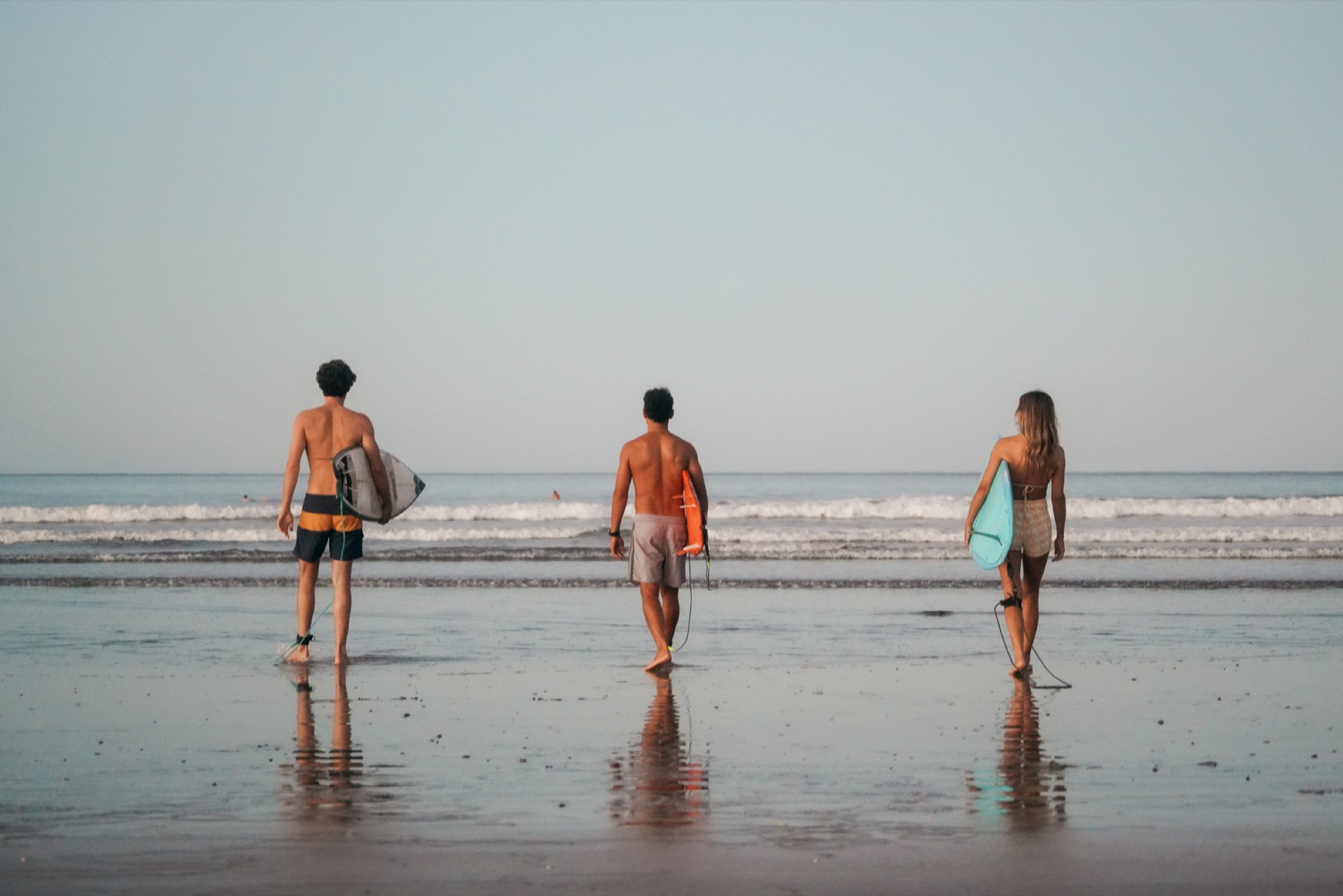 Three surfers walking to the water at golden hour, boards under their arms