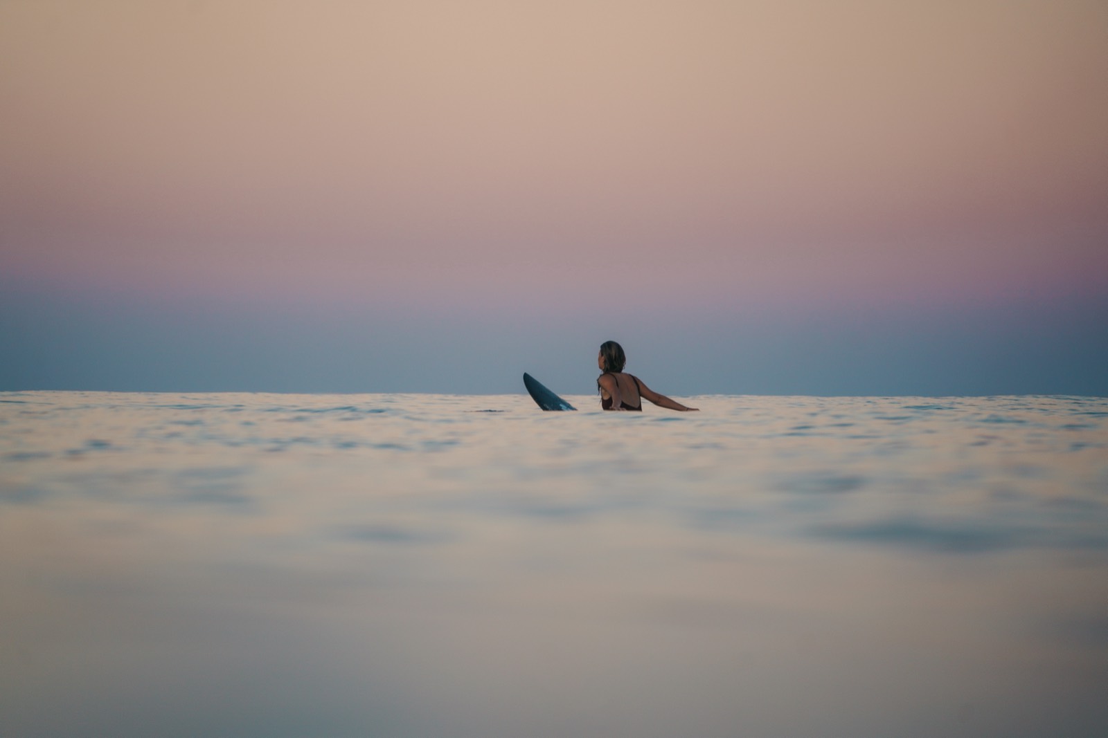 A lone surfer resting on the water at dusk under a pastel sky